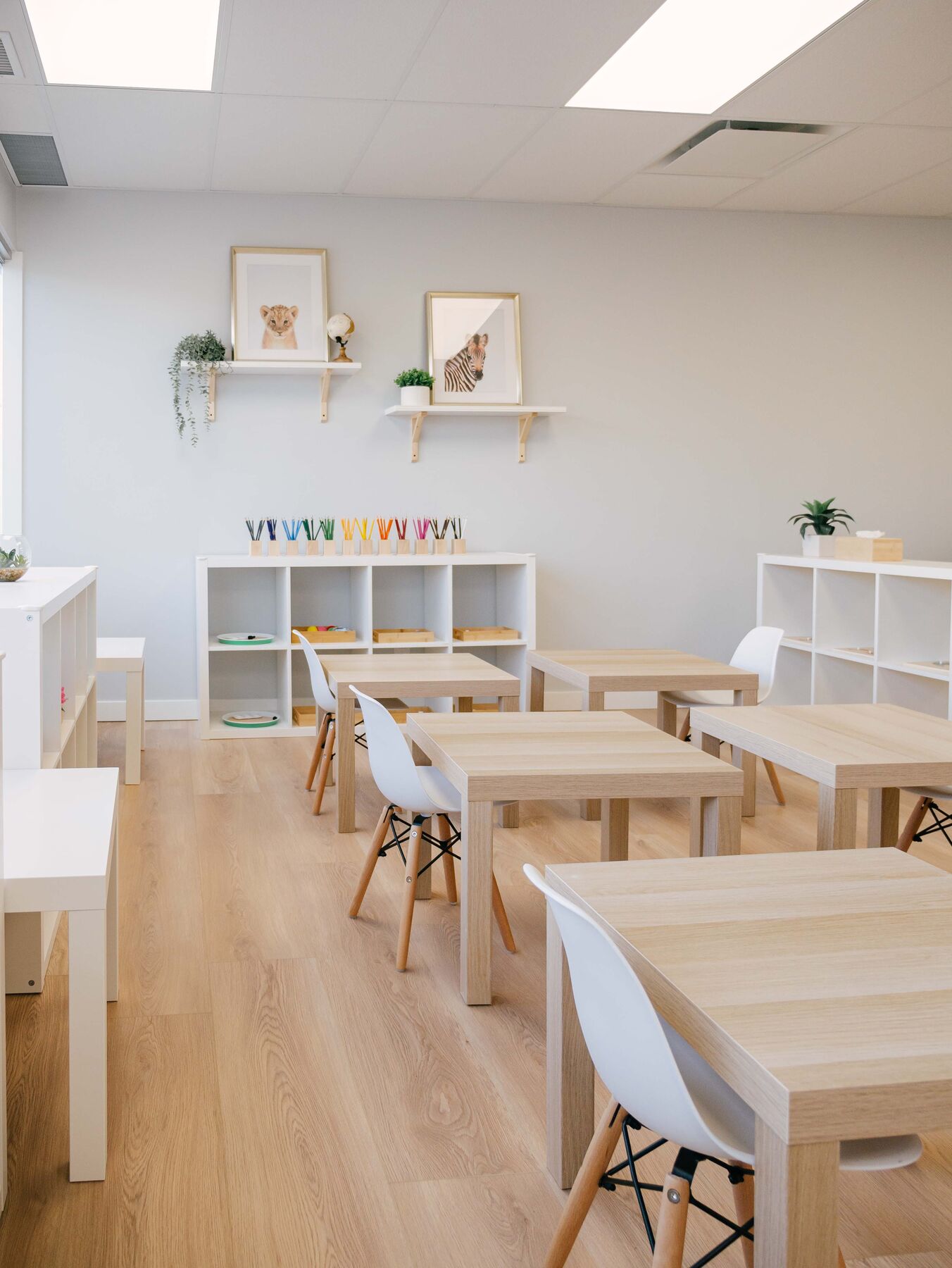 A calm classroom with pale walls, uncluttered white shelving, framed animal prints and child-sized tables.