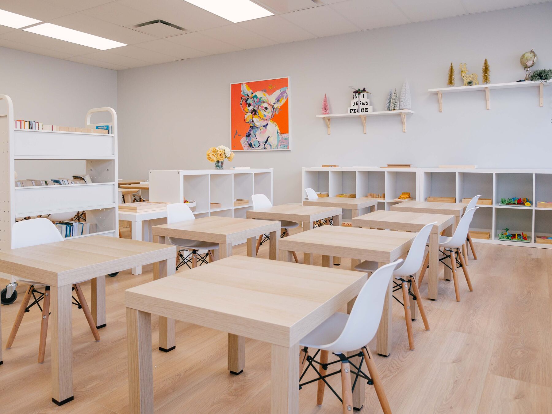 A wide view of a classroom with several clusters of child-sized tables and chairs beside a window wall.