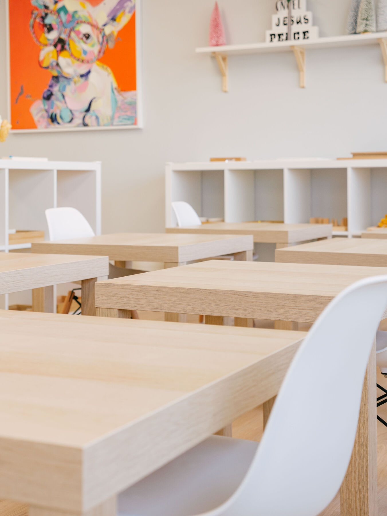 Pale wooden child-sized desks and white chairs arranged in small clusters across a classroom.