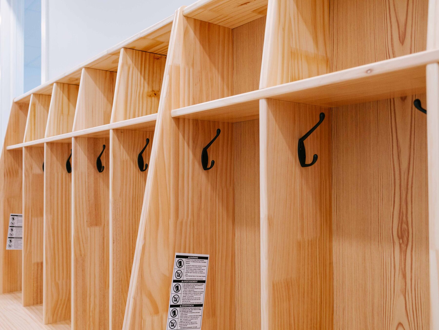 A close view of wooden cubby compartments with black coat hooks and name labels set at child height.