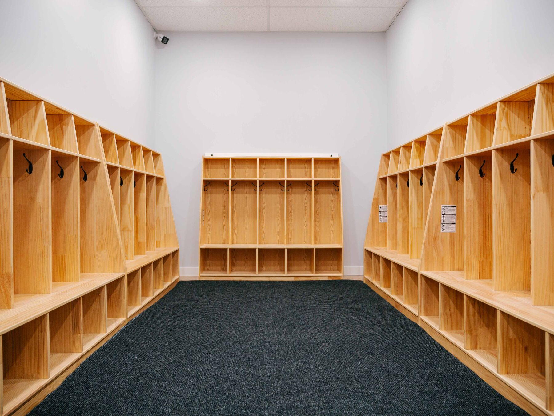A cubby room lined on both sides with solid wood cubbies and coat hooks above dark commercial carpet.