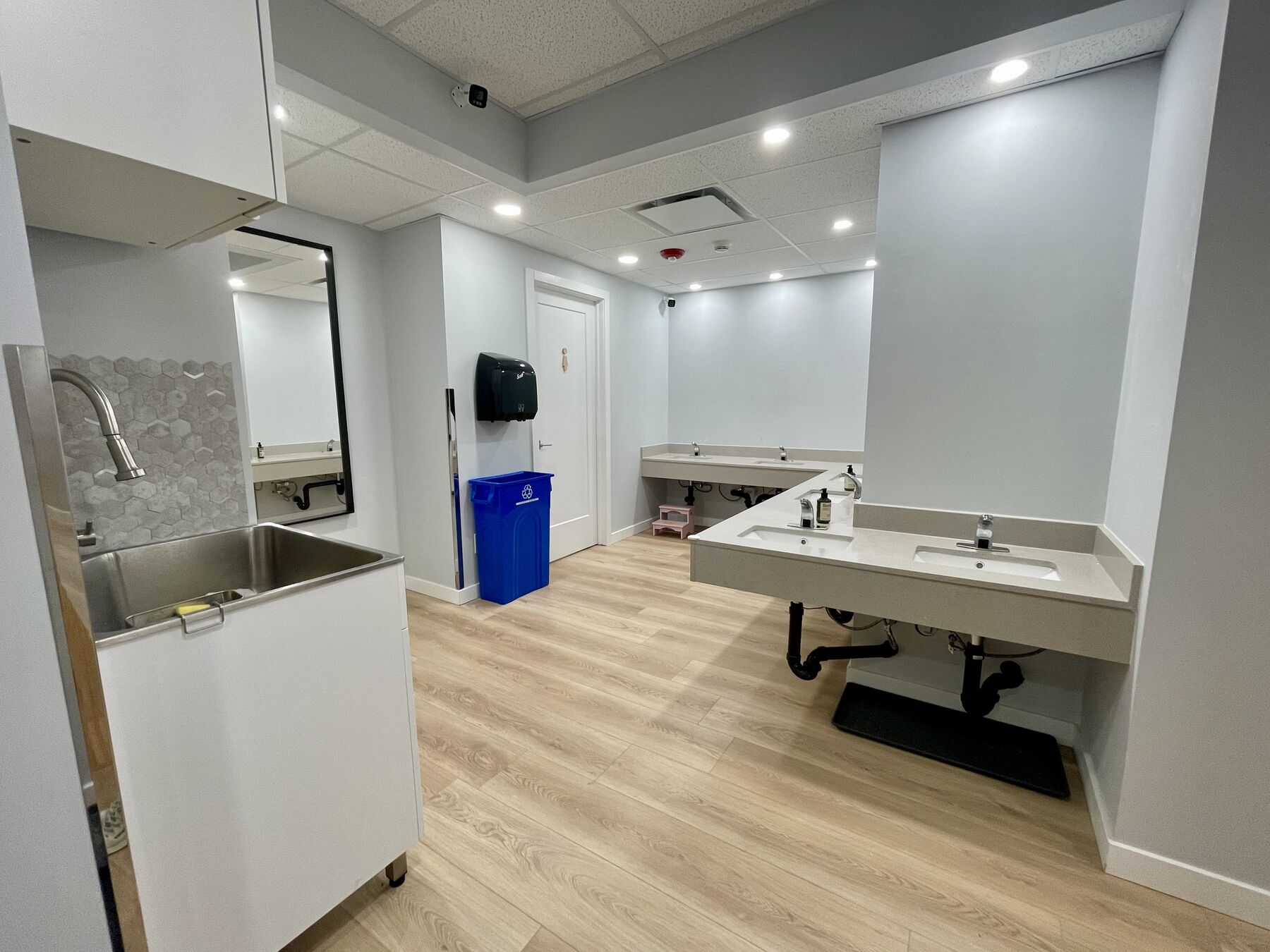 A childcare washroom with counter-mounted basins at child height along the wall and a deep stainless utility sink on castors.