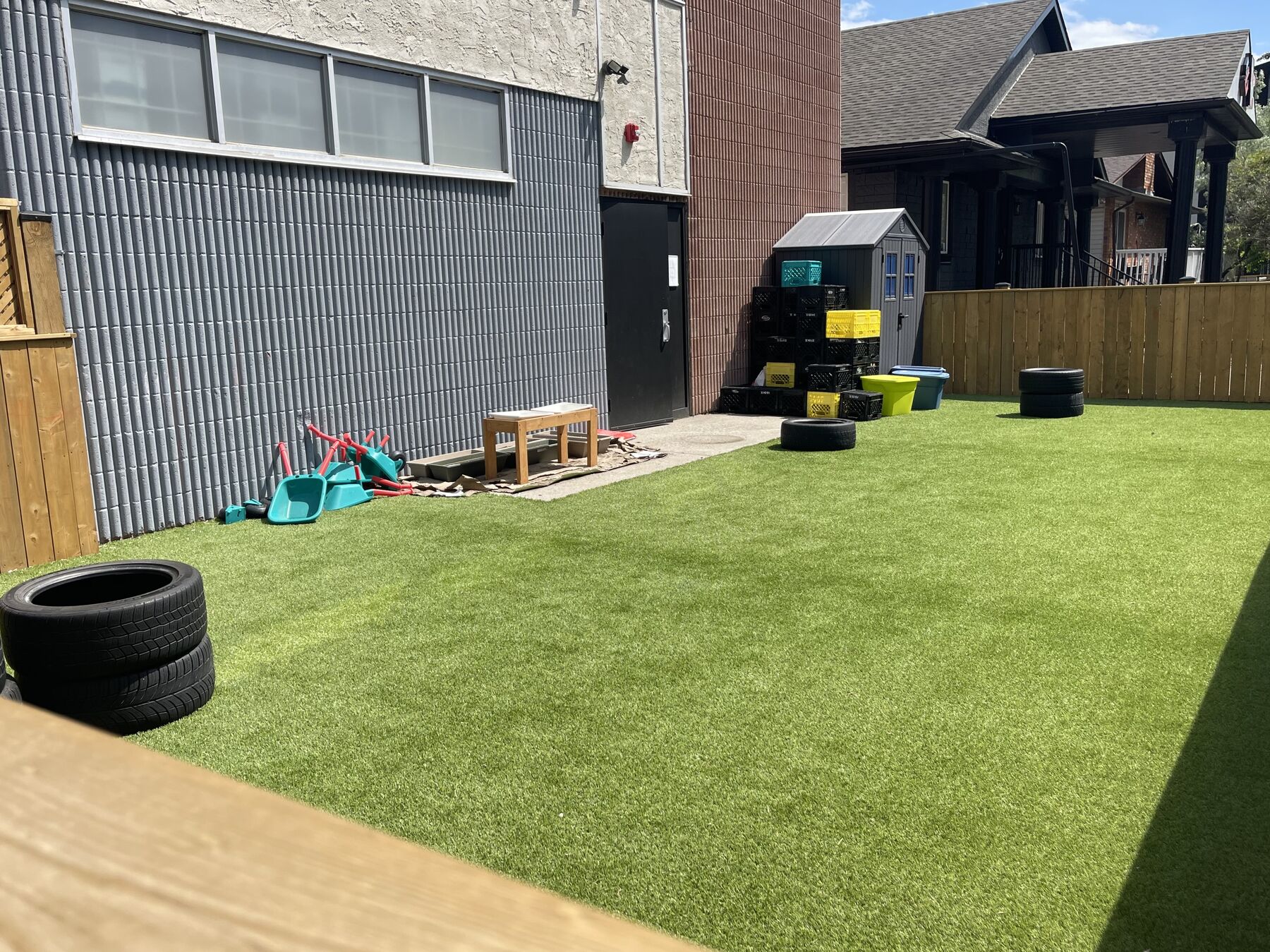 A fenced outdoor yard with all-weather green turf, loose tyres and a small climbing structure.