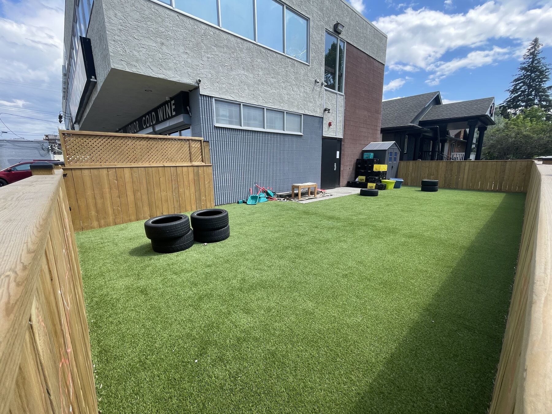 The turf yard seen from one corner, with the building along the far edge and wooden fencing closing the remaining sides.